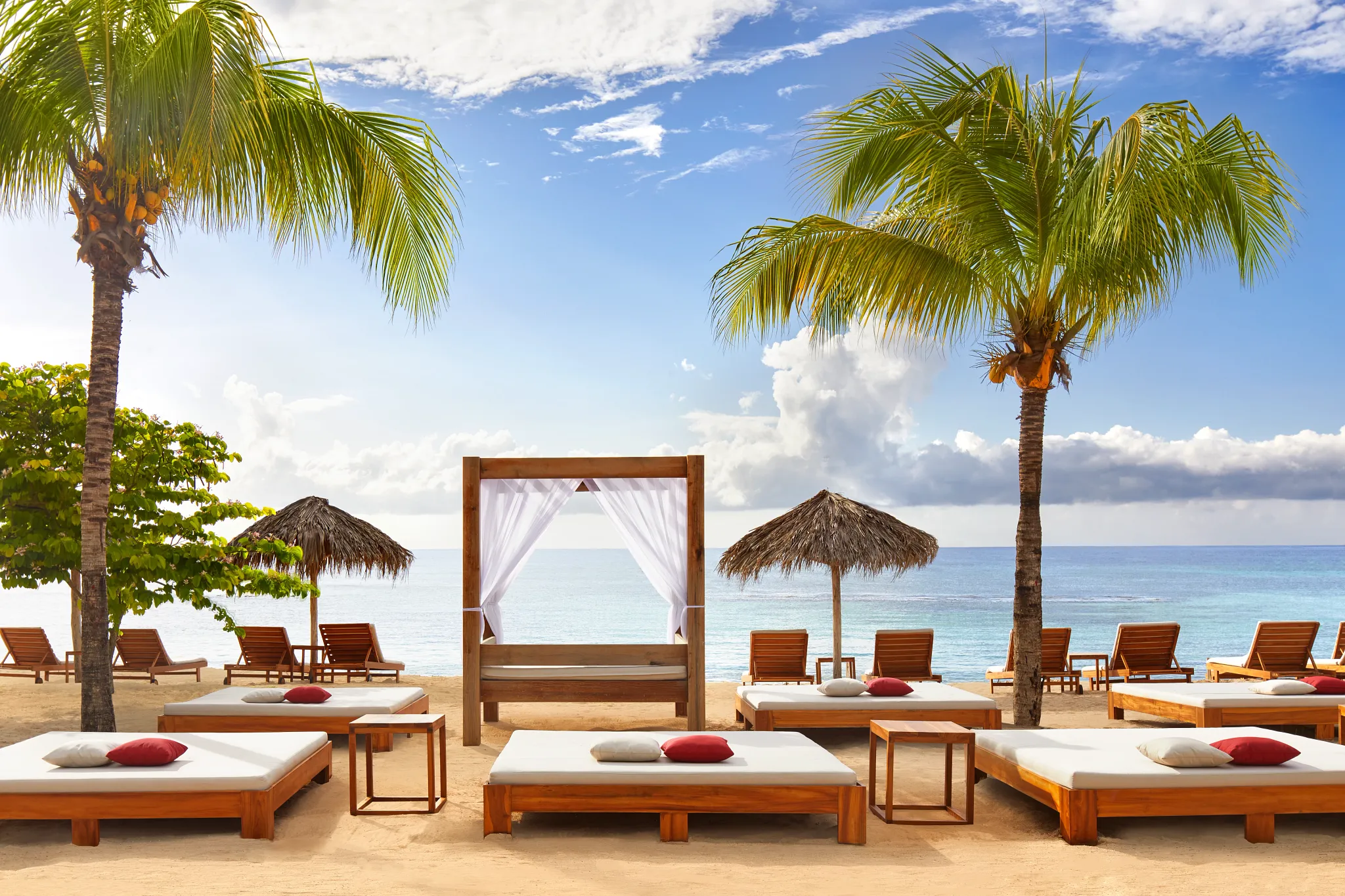 Luxury beach cabanas at Breathless Montego Bay set along the sandy shoreline with palm trees and ocean views.